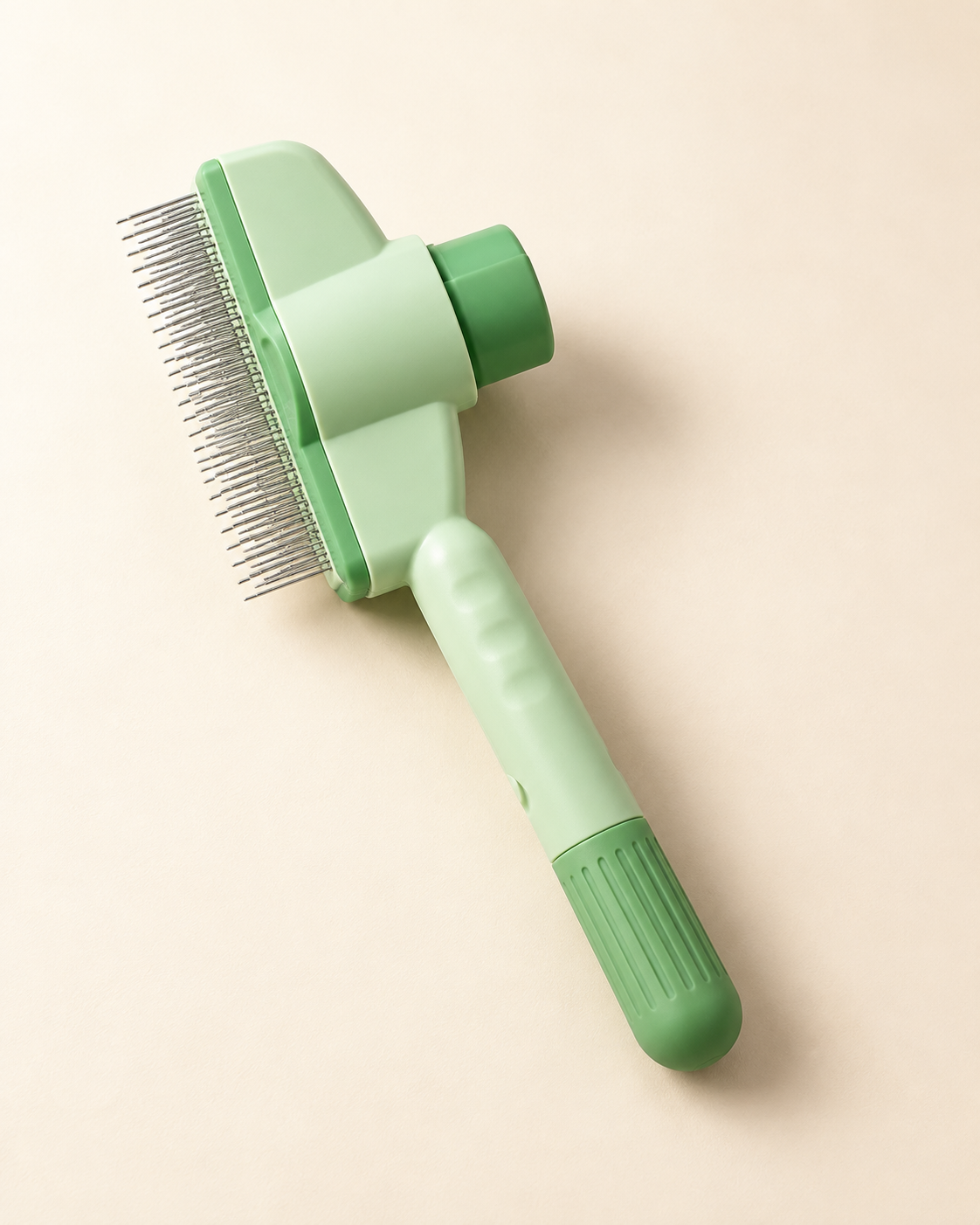 Mint-green self-cleaning grooming comb with fine metal pins and a push button on an ivory background.