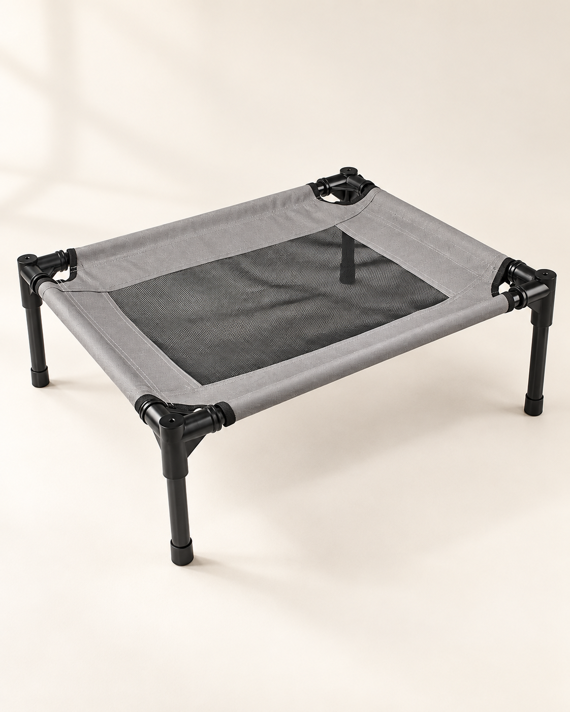 Compact gray elevated pet cot with black mesh sleeping panel, black frame and four legs on ivory.